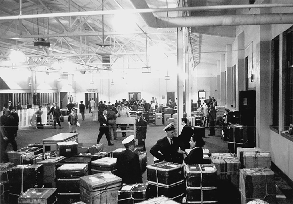 Image archivistique de grand hall d'immigration rempli d'officiers, passagers et bagages.